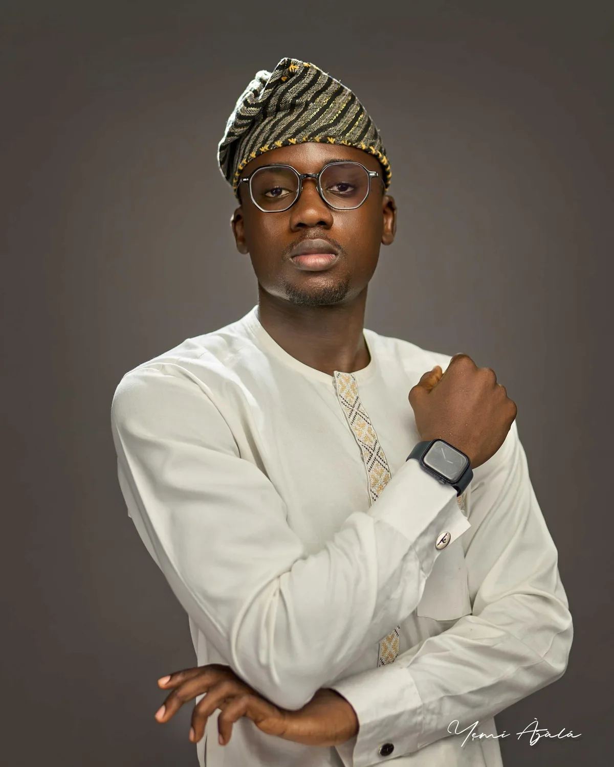 Portrait of Abubakar Adeshina wearing a white kaftan, a patterned fila cap and round glasses